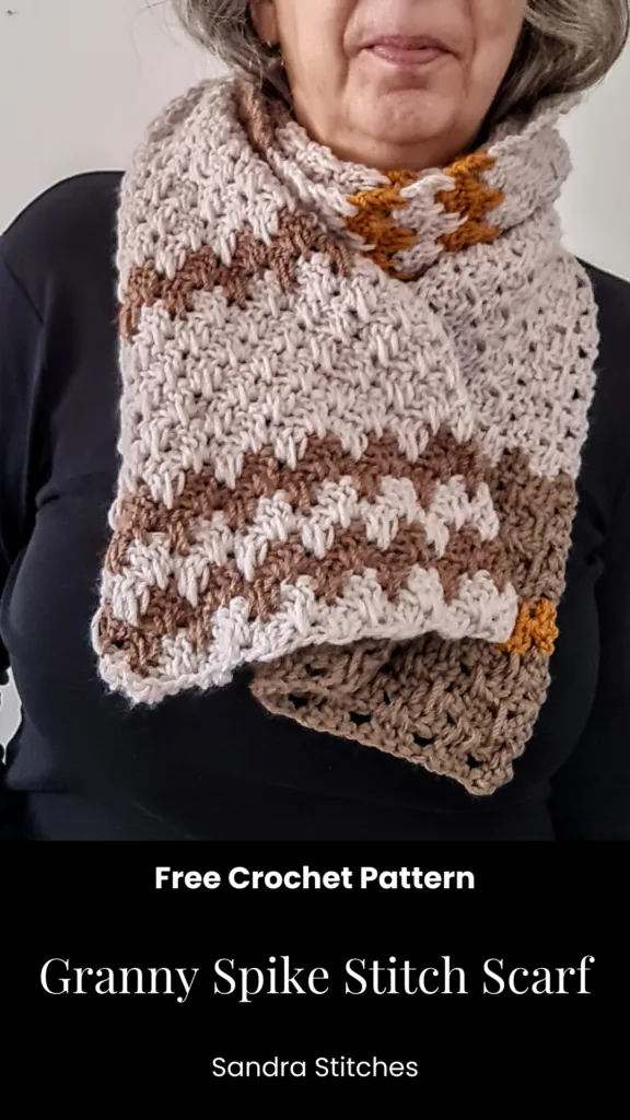 The image shows a crocheted scarf with a textured stitch pattern. It is beige and brown in color, with stripes of a mustard yellow accent color. The scarf appears to be modeled by an older woman with gray hair. The text overlay provides the title "Granny Spike Stitch Scarf" and indicates that this is a free crochet pattern