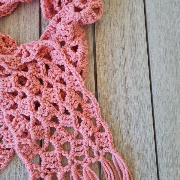 Coral pink lacy crochet scarf with shell pattern and long fringe displayed on white mannequin, featuring an airy diamond mesh design throughout