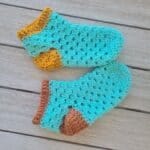 A finished pair of green and gold crochet granny slippers held up together