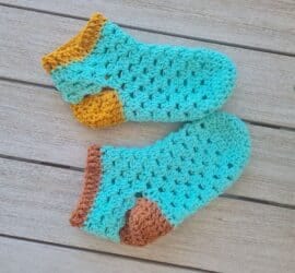 A finished pair of green and gold crochet granny slippers held up together