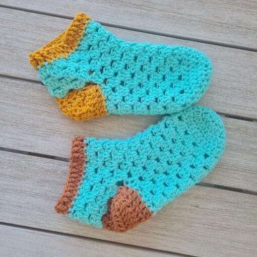 A finished pair of green and gold crochet granny slippers held up together
