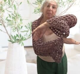 A woman wearing a crochet mesh shrug with bell sleeves the open Y stitch fabric draping softly over her shoulders