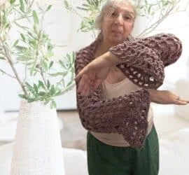A woman wearing a crochet mesh shrug with bell sleeves the open Y stitch fabric draping softly over her shoulders