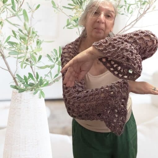 A woman wearing a crochet mesh shrug with bell sleeves the open Y stitch fabric draping softly over her shoulders