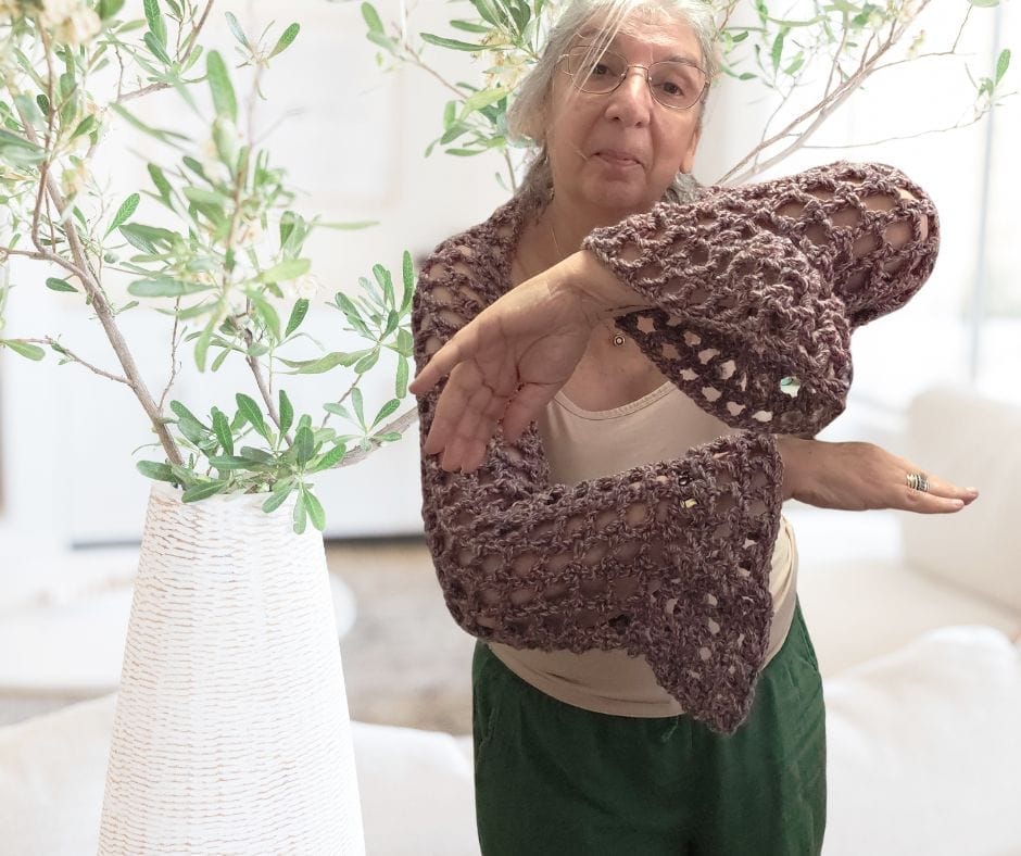 A woman wearing a crochet mesh shrug with bell sleeves  the open Y stitch fabric draping softly over her shoulders