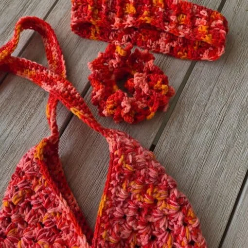 Three finished summer crochet projects in pink, orange, and peach variegated yarn, an envelope bag, a coral scrunchie, and an open headband, arranged as a matching set Bag